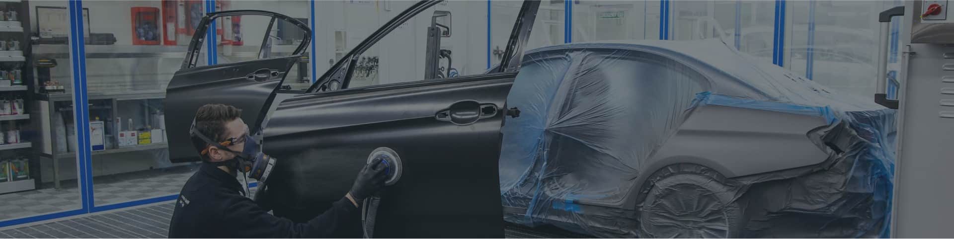 Painter working on a car door inside a spray booth